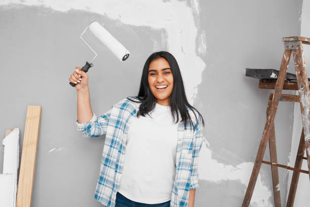 istock Young Indian woman poses with paintbrush roller getting ready to paint wall 1459953502