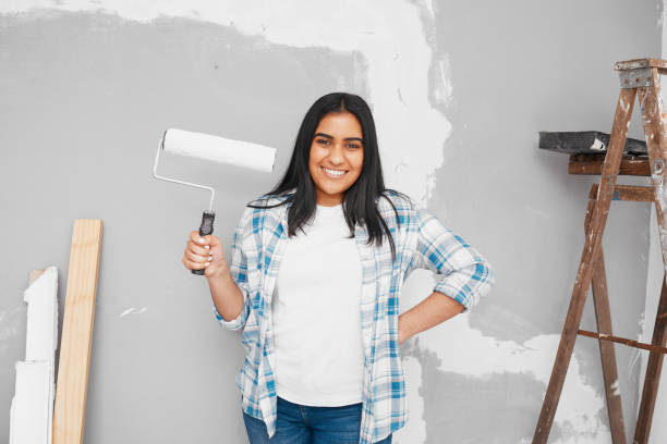 istock Young Indian woman poses with paintbrush roller getting ready to paint wall 1459953525
