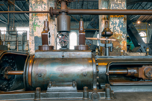 Fragment of steam engine from 1903. Important part of technological line in historical factory. Huge piston and \ncentrifugal regulator. Fragment of \nflywheel in the background.