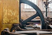 Fragment of steam generator used for steam engines in historical factory from 1903. Huge flywheel and yellow casing of the machinery. Rusted wall in the background.