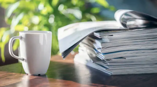 Magazine pile and coffee cup on table in cafe or home living room background