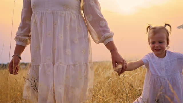 Tracking, slow motion of mother and daughter walking down a meadow while holding hands