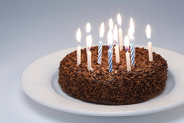 A brown birthday cake on a white plate with several candles stock photo