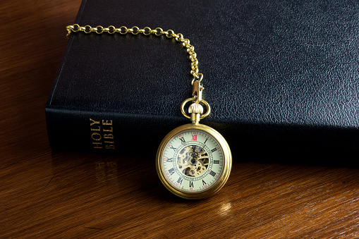 Vintage pocket watch and chain with a christian bible on a polished wooden surface