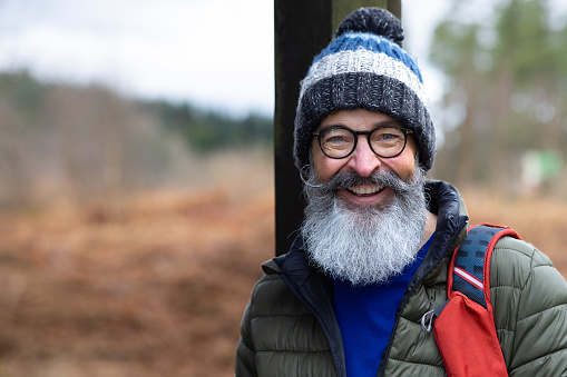 Portrait of a man standing outdoors while on a walk in Northumberland, North East England. He is smiling at the camera in the countryside.  He is dressed warmly with a hat on.