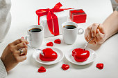 A couple in love is sitting at a table holding hands. A gift for a loved one. Coffee and red heart-shaped cakes.