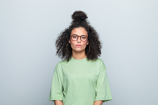 Confident young woman wearing green t-shirt and eyeglasses looking at camera. Studio shot against grey background.