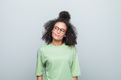 Young woman wearing green t-shirt and eyeglasses looking up. Studio shot against grey background.