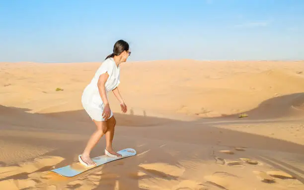 Young women sand surfing at the sand dunes of Dubai United Arab Emirates, sand desert on a sunny day in Dubai.