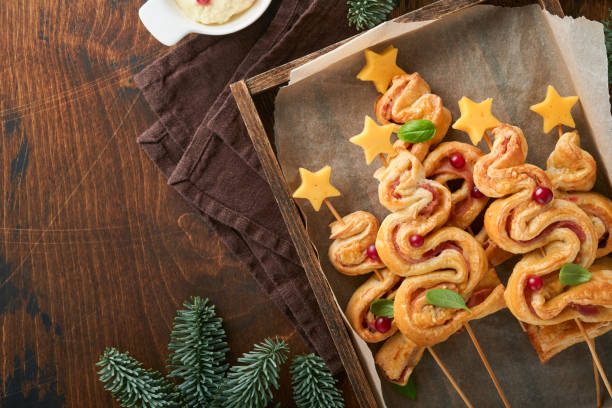 istock Christmas or New Year appetizer. Christmas tree shape puff pastry buns with cheese and ham. Group of Christmas tree shapes on wooden board. Festive idea for Christmas or New Year dinner. Top view. 1459971338