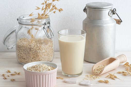 plant based oat milk in a glass, cereal grain and bottle around, healthy plant milk