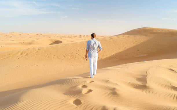 junge männer zu fuß in der wüste von dubai, sanddünen von dubai vereinigte arabische emirate - dubai united arab emirates traditional culture camel stock-fotos und bilder