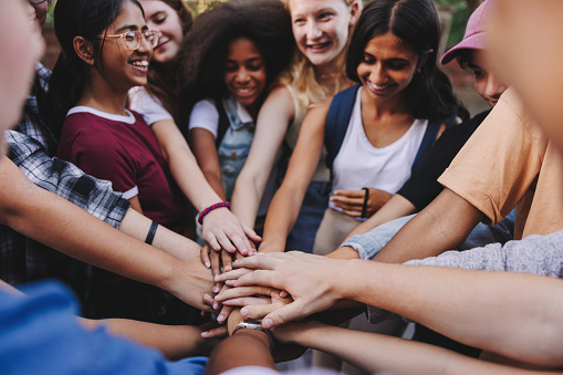 Teenagers smiling happily while putting their hands together in a huddle. Group of multicultural students making a stack of hands