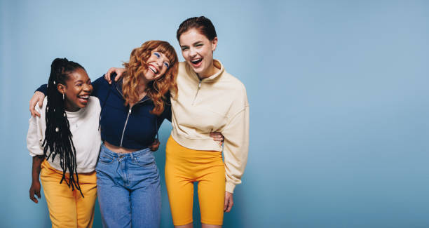 Girls having fun together in a studio Multiethnic young women laughing and having fun while embracing each other. Group of cheerful female friends enjoying themselves while standing against a blue background. mixed racial group of friendly children laughing together stock pictures, royalty-free photos & images