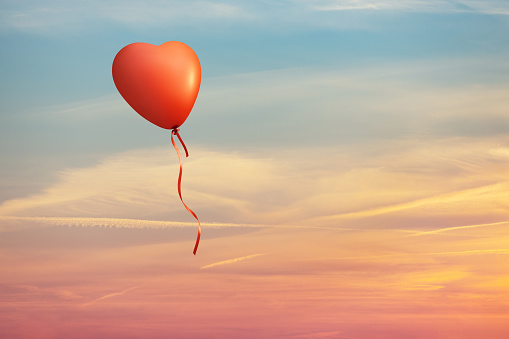 Heart shaped red balloon on colorful clouds sunset sky. This file is cleaned and retouched.