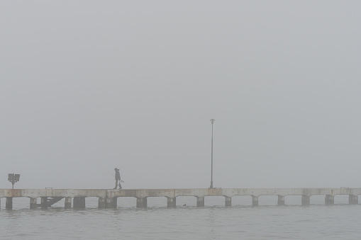 Pier with one man in distance on a foggy day.