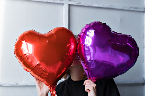 Two heart-shaped balloons red and purple on a white-gray background. Caucasian woman celebrating valentine's day. A note to your boyfriend. The concept of human emotions, facial expressions, relationships, romantic holidays. High quality photo