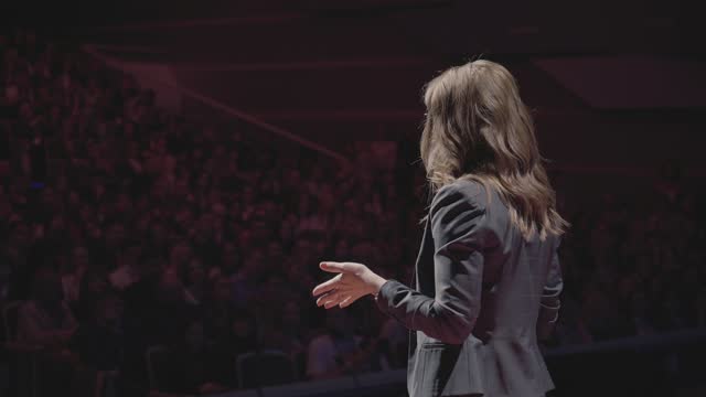 Elegant and Confident Business Woman Public Speaking at Modern Conference on Auditorium. Successful Coach Emotional Gesturing Talks from Stage Spectators at Forum. One Female in Suit Standing Close-up