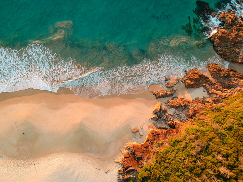 Drone footage  with a top down view of the waves crashing on the Tomaree National Park beach and coastline as the sun rises up.