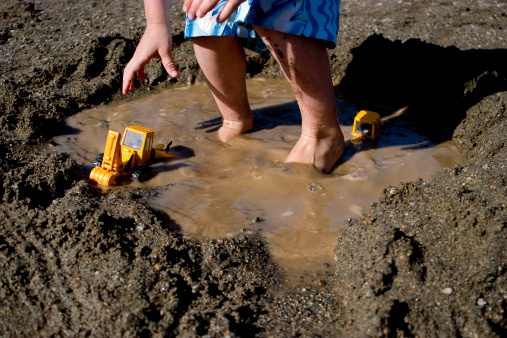 Child plays with toys at beach in puddle.
