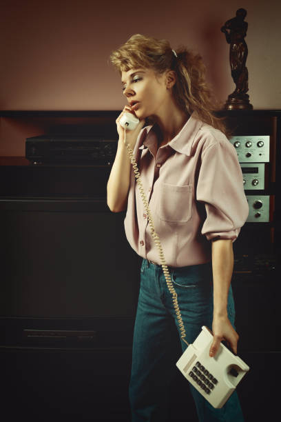 vintage lifestyle portret młodej blondynki na przełomie lat 80., 90., wystrój wnętrza, rozmowa przez telefon w salonie - shirt women pink jeans zdjęcia i obrazy z banku zdjęć