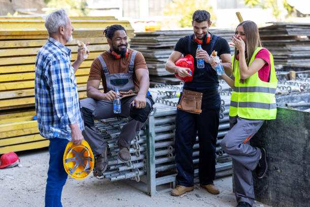A Multi-Ethnic Group of Construction Workers is Taking a Break and Eating. A Group of Multiracial Workers at the Construction Site is Taking a Break and Eating a Sandwich and Resting. construction lunch break stock pictures, royalty-free photos & images