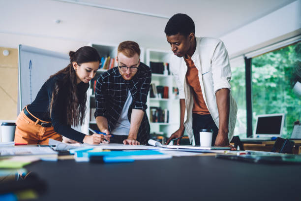 istock Group of smart casual developers working with project sketches for architect order, young colleagues collaborating at desktop table on blueprint illustrations discussing ideas and communicate 1459998295