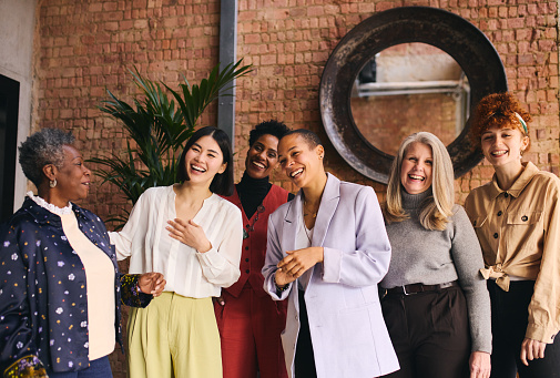 Portrait of cheerful multiethnic businesswomen laughing and smiling in office with exposed brick wall interior