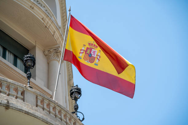 flagge von spanien mit roten und gelben farben, die an einem sonnigen tag mit blauem himmel im wind wehen - spain flag built structure cloud stock-fotos und bilder