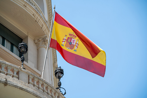 Flag of Spain with red and yellow colors waving in the wind during a sunny day with blue sky on summer