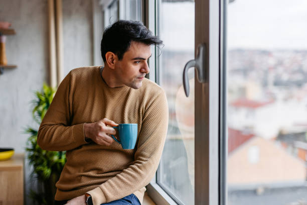 Young Man Drinking Coffee By The Window At Home