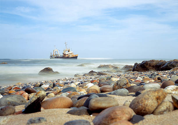 Round Beach Rocks With Shipwreck in the background, Namibia Taken with a Mamiya C220 on positive, 120, medium format film in between Swakopmund and Walvis Bay, Namibia. Used 3 Nuetral Density filters in the miday sun to achieve the motion blur. swakopmund photos stock pictures, royalty-free photos & images