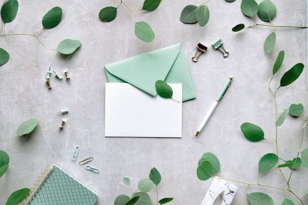istock Mint green postal envelope, white card, pen and office stationary. Eucalyptus twigs on stone, overhead view.Delicate green silver dollar eucalyptus leaves. 1460004139