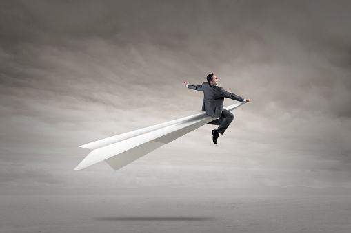 A businessman holds on as he rides in a paper airplane that is taking off.