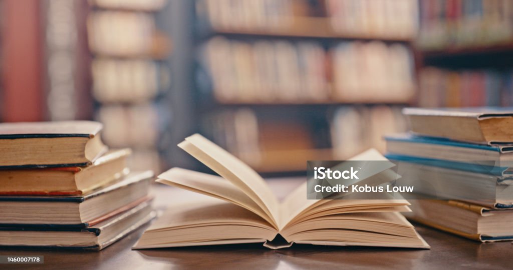 Library, books on table and background for studying, learning and research in education, school or college. Reading, philosophy and open, vintage or history print book, university blurred background Book Stock Photo