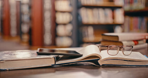 istock Tablet, library background and books on table studying, learning or education with glasses. Reading knowledge, philosophy research and university with vintage, history or print textbook on a desk 1460007437
