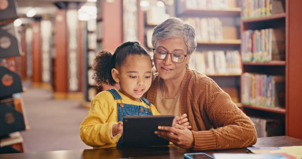 istock Child, black family and tablet library for online learning development with education and reading. Senior woman teaching girl kid while streaming website, ebook and books to learn knowledge together 1460008006