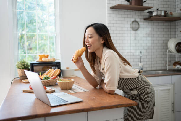 istock Adorable woman using laptop for recipe while preparing food in kitchen. 1460008330