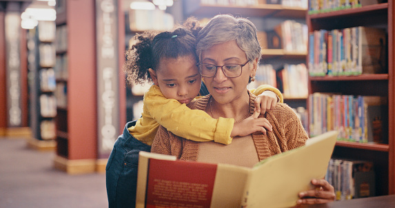 Lectura, educación y abuela con nieto en la biblioteca, abrazarse y vincularse mientras están sentados juntos. Aprender, contar cuentos y abuela enseñando a la niña, relajarse y disfrutar de los libros, cuentos y desarrollo infantil photo