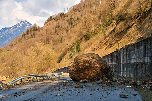 A huge rock fell from the mountains onto the road, destroying the asphalt and blocking half of the roadway.