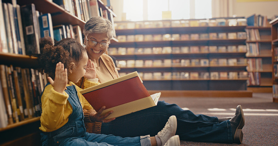 Education, book and grandmother with grandchild on library floor, reading and happy, smile and playful. Learning, books and girl with grandma, excited and cheerful for storytelling, fantasy and bond
