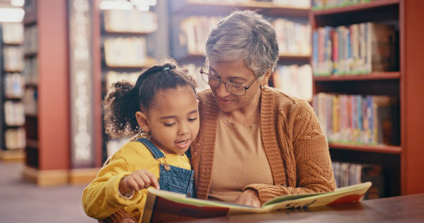 Library, book and grandma with grandchild, learning and reading while having fun together. Storytelling, education and grandmother relax with girl, teaching and bonding, content or child development