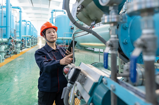 An Asian female engineer uses a tablet computer to record equipment in a chemical plant