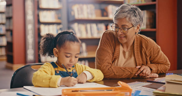 istock Help, book and senior with child learning, teaching and writing in education, language and school library. Creative development, kindergarten and support of people, grandmother or teacher helping kid 1460011131