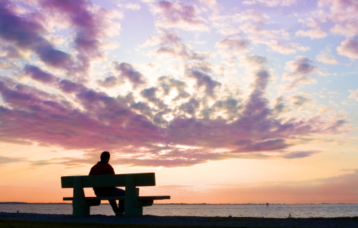 silhouette of thinking man on bench by sunset