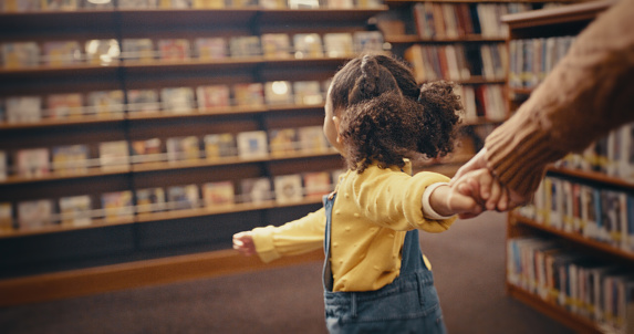 Biblioteca, educación y una niña tomada de la mano mientras guía a una mujer a través de una librería para leer o aprender. Niños, caminatas y libros con una niña que busca un libro para leer para el desarrollo photo