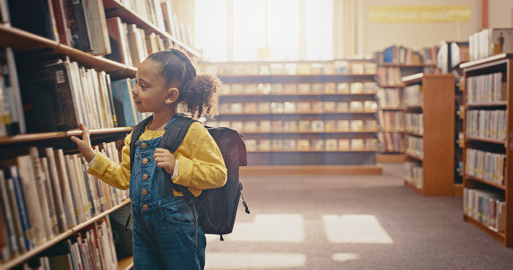 Young girl in library, book choice and reading for knowledge, education and learning for school. Study, kindergarten student and female kid search bookshelf for story, academic development and growth