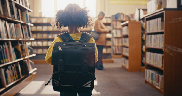 istock Young girl in library with backpack, books and reading for knowledge, education and learning for school. Study, kindergarten student and female kid back view, bookshelf with academic development 1460016886