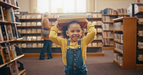 Black girl holding books, library and happy with education, learning and story time with fun, smile and knowledge. African American female child, kid and young person with book, happiness and youth