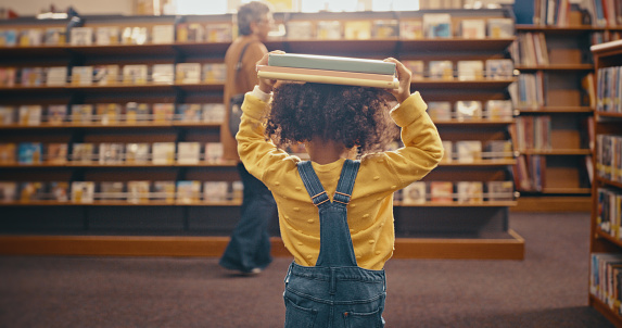 Niña, biblioteca y llevar libros en la cabeza caminando a la estantería de lectura terminada en la tienda. Niña, niño o niño pequeño hecho, completado o terminado con el tiempo de libro de cuentos en la tienda photo